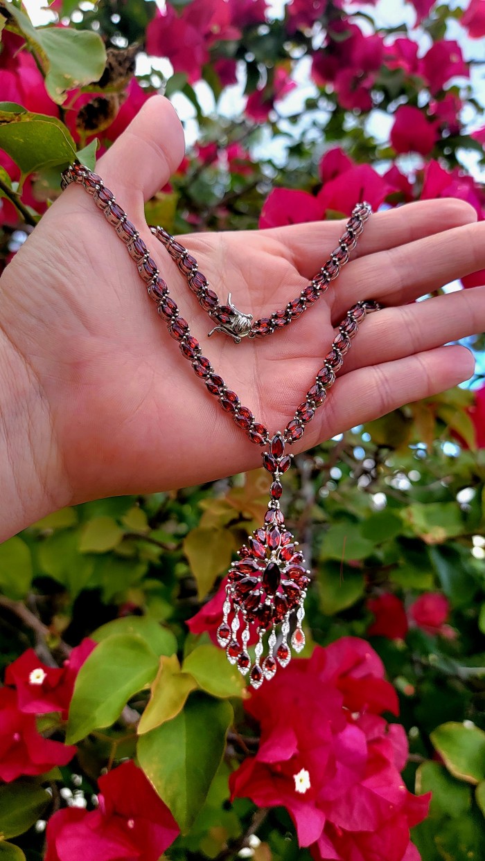Red Royalty Authentic 185.5 carat authentic Tanzania Garnet .925 Sterling Silver brilliantly handcrafted necklace - Worn on hand, red Tanzanian garnet necklace against pink flowers.