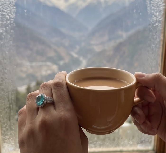 Elizabeth oval cut 10.4 carat Colombian Emerald .925 Sterling Silver dipped in rhodium handcrafted Ring size 7 1/4 - Emerald ring worn on hand while holding a cup, mountain view in background.