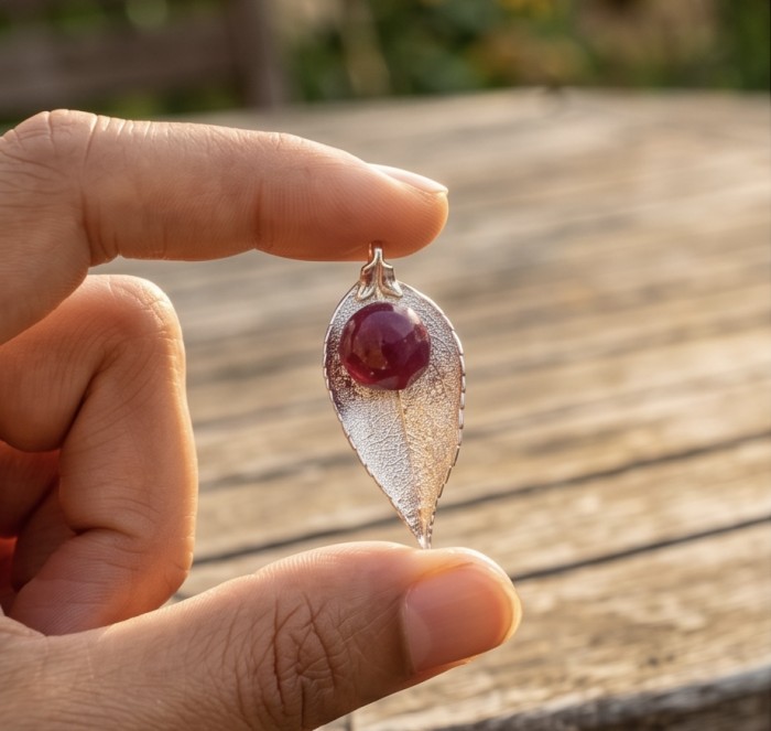 Stylish REAL Leaf dipped in gold Ruby .925 Sterling Silver and Copper Pendant - Close-up of leaf-shaped pendant with ruby on wooden background