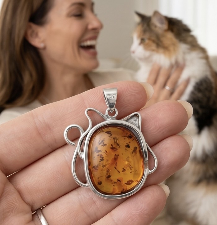 Cat - Prehistoric Authentic Baltic Amber .925 Sterling Silver beautifully handcrafted Pendant - Close-up of cat-shaped amber pendant in hand, woman and cat in background.