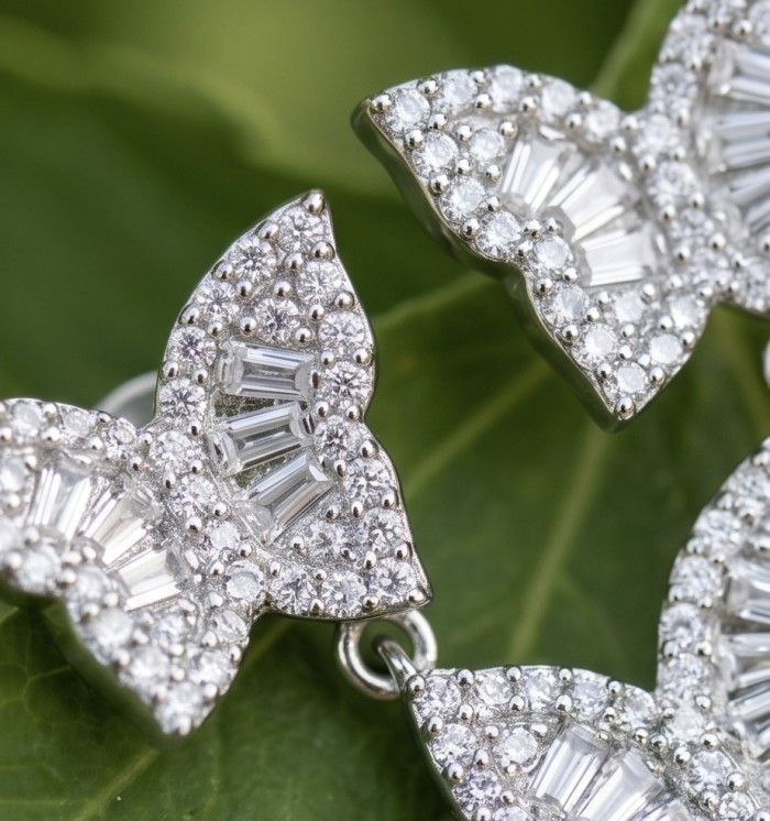 Four Butterflies natural 7.5 carat White Topaz .925 Sterling Silver handmade Statement Earrings - Close-up of butterfly-shaped white topaz earrings on a leaf background.